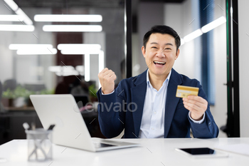 Successful businessman celebrating with credit card at office