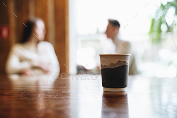 Two People Engage in Conversation Behind Coffee Cup on Wooden Table