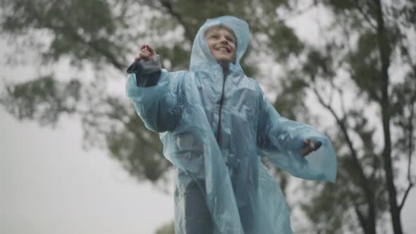 Portrait of Happy Joyful Caucasian Boy Jumping and Cheering Rain Outdoors