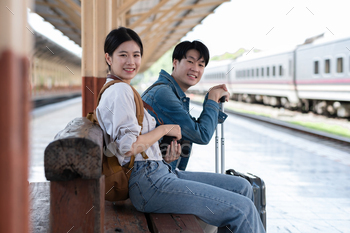 A young Asian couple waits for their train together at the train station, waiting to travel.