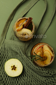 Glasses with apple cider and apple slice on bag on green background, top view
