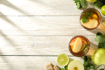 Glasses with apple cider, mint branches and apples on light wooden background, space for text