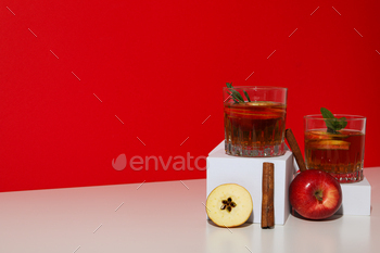 Glasses with apple cider, apples and cinnamon sticks on red background, space for text