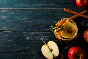 Glasses with apple cider and red apples on towel on wooden background, space for text