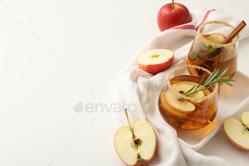 Glasses with apple cider and apples on towel on white background, space for text