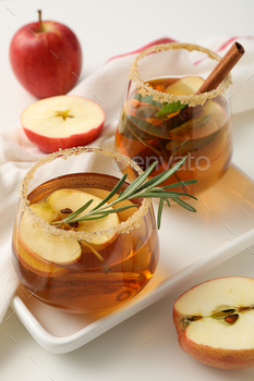 Glasses with apple cider and apples on towel on white background, close up