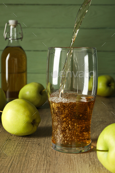 Glass and bottle with apple cider and green apples on wooden table on green wooden background