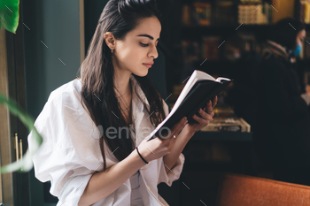 Concentrated woman with book studying in library