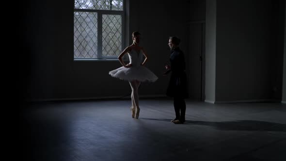 Graceful Ballerina in White Tutu Rehearsing in Darkness with Choreographer in Black Dress