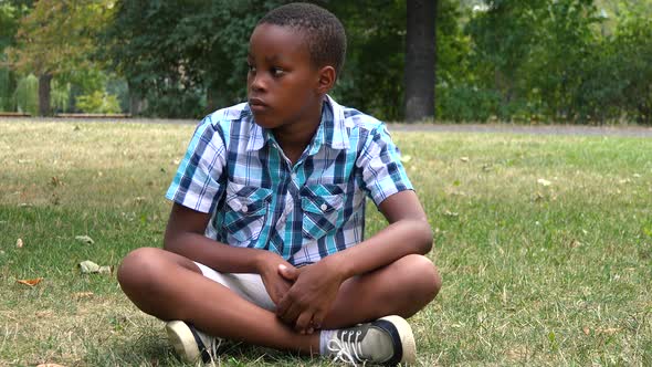 A Young  Black Boy Sits on Grass in a Park and Looks Around