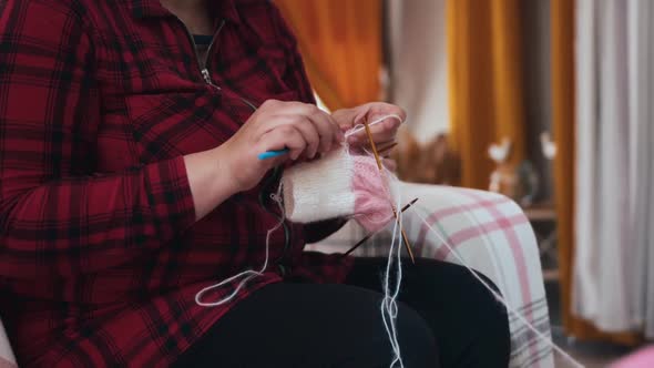 A Woman Knits Little Clothes with Knitting Needles