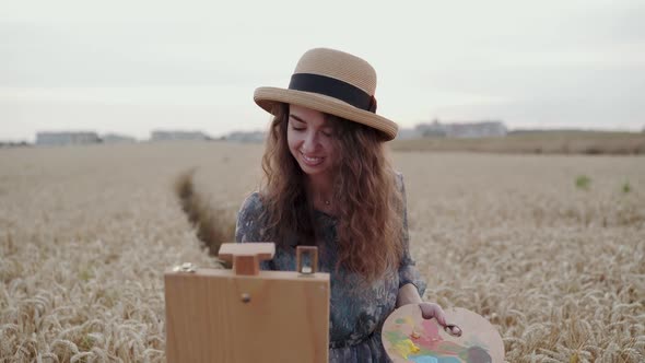 Elegant Lady Painting on Canvas with Smile on Face Among Ripe Wheat Field