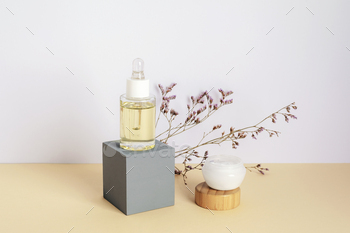 Cosmetic serum and cream in a jar and purple kermek flowers on beige table. Natural cosmetics