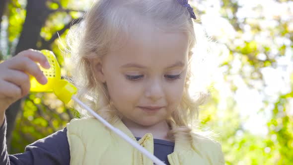 Close-up Portrait of a Charming Blond Girl Blowing Soap Bubbles and Smiling