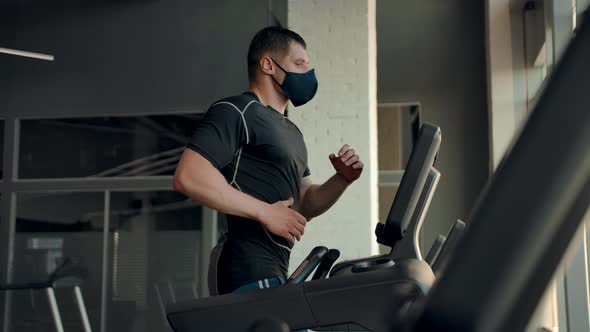 A Professional Athlete in a Protective Mask Runs on a Treadmill in the Gym