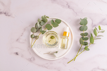 Natural cosmetic eucalyptus oil in a bowl and cosmetic bottle on an tray among eucalyptus twigs.