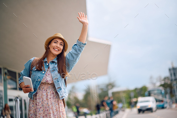 Young happy woman hailing for a taxi at airport.