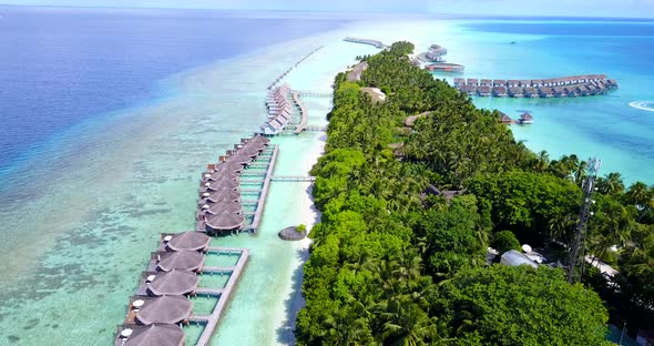 Bungalows in line over shallow turquoise lagoon with coral reefs connected by wooden piers to white