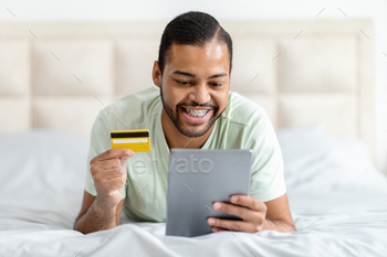 Man Laying on Bed With Credit Card and Tablet