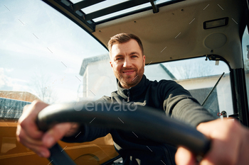 By the steering wheel. Man is with tractor. Agricultural worker