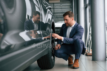 Checking the wheel. A businessman is in a car dealership