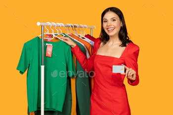 Woman Holding Credit Card in Front of Rack of Clothes