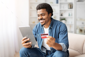 Man Sitting on Couch Holding Credit Card and Tablet