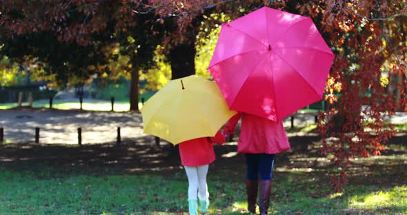 Mother and daughter walking together in park under umbrella