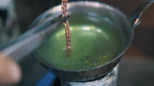 Jeweler Puts Gold Chain Into Boiling Green Liquid Closeup