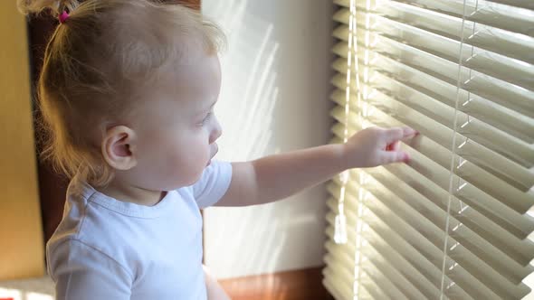 The child pushes the blinds and looks at the street through the gap