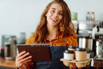 Handsome manager of coffee shop with curly hair tablet in hands gives takeaway coffee in coffee shop