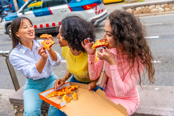 Women sharing pizza sitting in the street