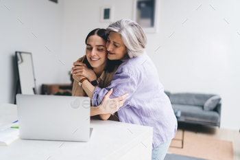 Smiling elderly mother embracing young daughter while using computer