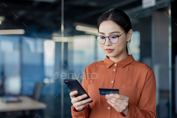 Businesswoman using smartphone and credit card in office
