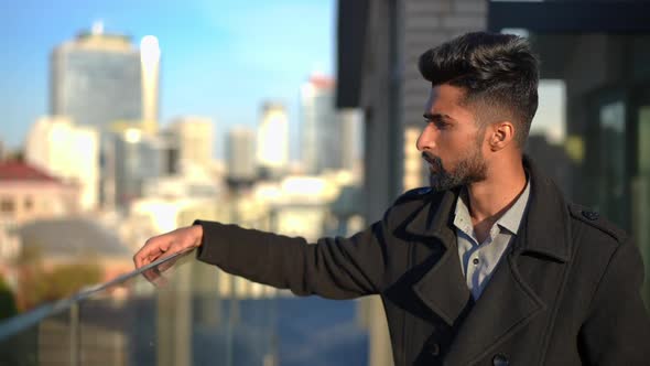 Troubled Anxious Middle Eastern Man Hitting Glass Fence on Rooftop Looking Away at Urban City