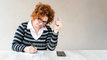 A woman with red hair and glasses is writing in a notebook.
