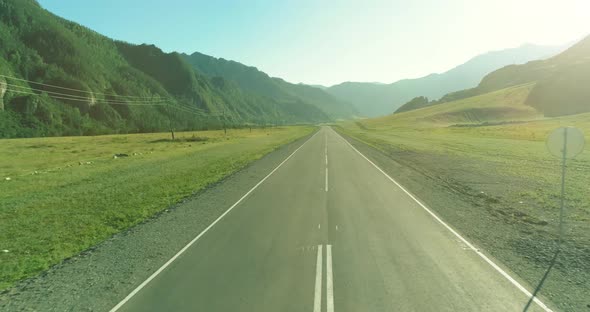 Aerial Low Air Flight Over Mountain Road and Meadow at Sunny Summer Morning.