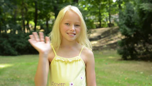 Little Cute Happy Girl Stands in the Park and Waves To the Camera - Greeting