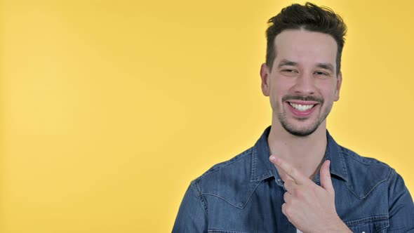 Portrait of Young Man Pointing at Product, Yellow Background