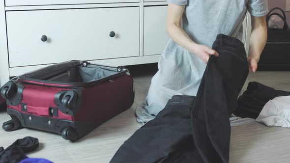 Unrecognizable Female Hands Grey Dress Packing Black Trousers in Red Suitcase