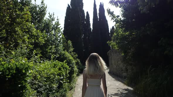 Slender Girl in White, Short Dress Enters a Maze of Greenery.