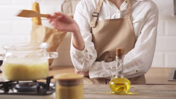 The Hostess In The Kitchen Is Standing Happy Preparing Food. Waving A Hand Spatula For Cooking