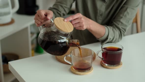 Woman in a Linen Shirt Pours Tea Into Two Transparent Cups