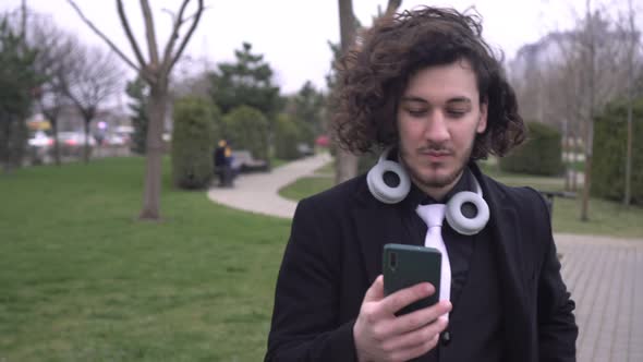 Young Modern Man with a Smartphone Walks in the Park in Spring