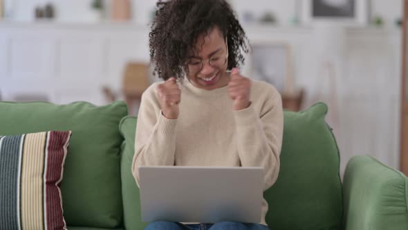 Successful Young African Woman with Laptop Celebrating on Sofa 