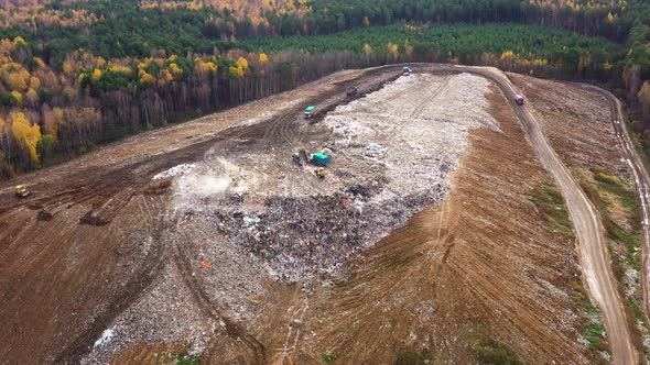 Landfill. A Huge Pile of Garbage Surrounded By Forest. Garbage Trucks Carry Garbage To a Landfill.