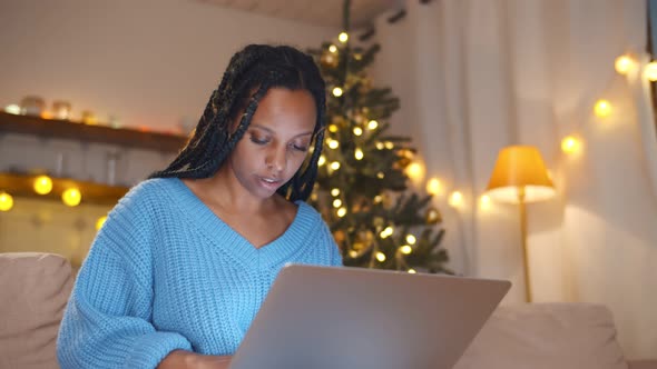 Young African Woman at Home in Christmas Time Surfing Internet on Laptop