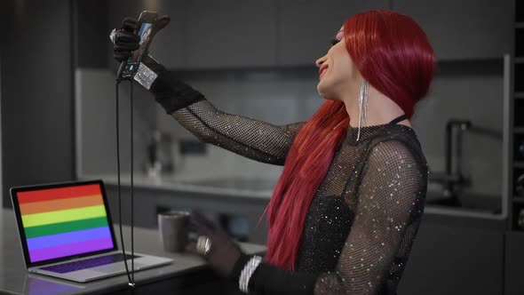 Side View Confident Caucasian Woman in Red Wig with Makeup Taking Selfie Sitting at Home with Laptop