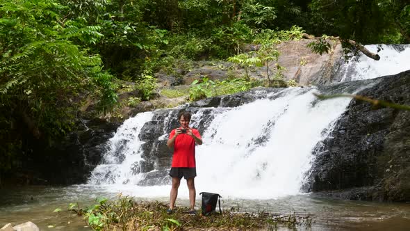 Young Traveler Man Using Smartphone and Shooting Photo or Video at Waterfall