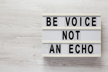 'Be voice not an echo' on a lightbox on a white wooden background, top view.
